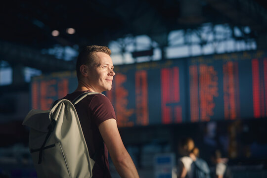 Traveling By Airplane. Portrait Of Man Walking Through Airport Terminal Against Flight Information Board..