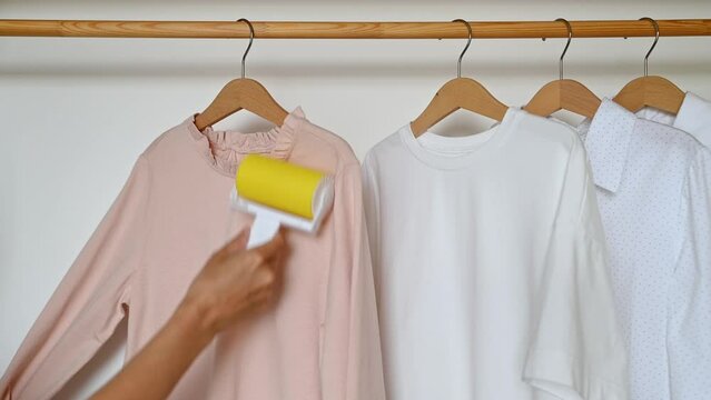 A woman's hand cleans clothes with a reusable clothes roller hanging on a wooden hanger.