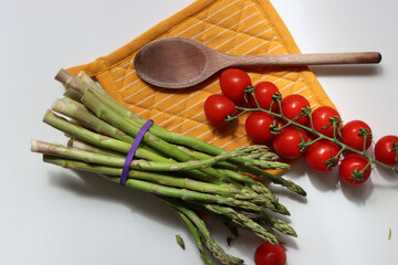 Fresh cherry tomatoes and green raw asparagus on white background with copy space. Eating fresh concept. Vegetarian meal ingredients. 