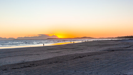 Fototapeta na wymiar Beach Ocean Sea Water Coastline as Sun is going down distant people walking the beach silhouette landscape