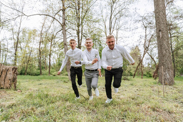 The groom and his friends pose against the background of the forest. not a large company of people having fun. Smiling boys run through the forest and rejoice together with the bridegroom