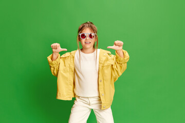 Confident child. Photo of little girl wearing stylishly, listening to music over green background.
