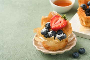 Phyllo or filo pies with fresh berries strawberries and blueberries, cheese filling topped with fresh mint on white plate. Homemade Filo pastry paskets. Delicious filo pastry dessert.