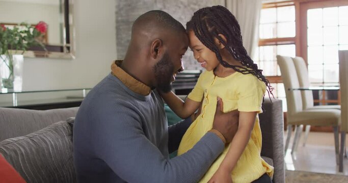 Happy african american daughter and father embracing and talking on sofa