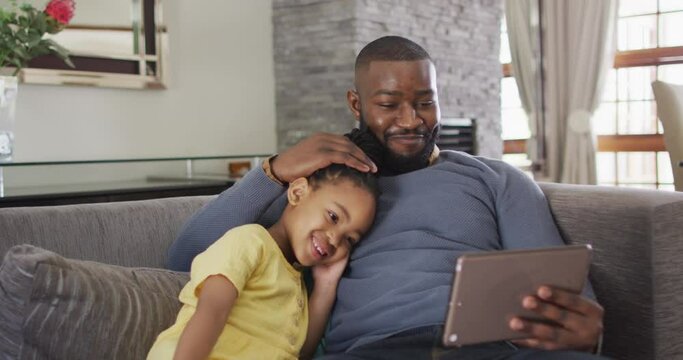 Happy african american daughter and father using tablet on sofa