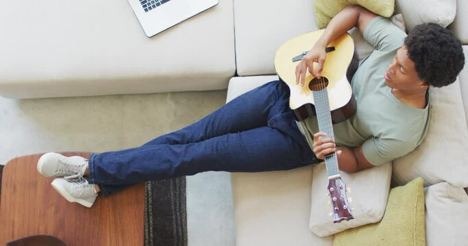 African american man plays guitar and singing, using laptop at home