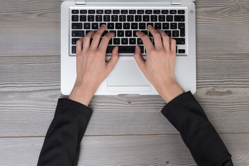 Overhead view of hands of a young adult wearing a jacket and typing on a laptop keyboard resting on...