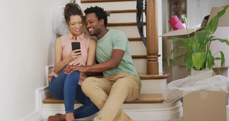 Happy biracial couple taking selfie on stairs of their new house - Powered by Adobe