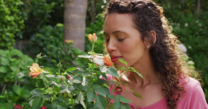Portrait of happy biracial woman smelling roses in garden