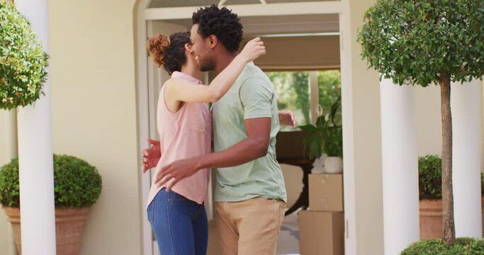 Happy biracial couple holding keys to new house and embracing with joy