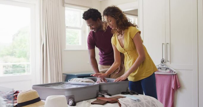 Happy biracial couple packing clothes into suitcase together, preparing for travel