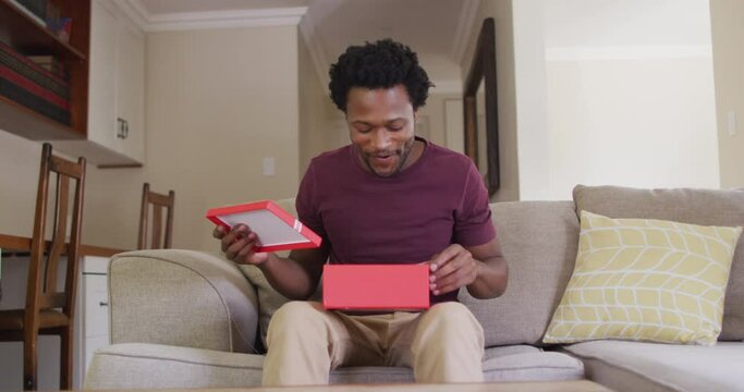 Happy biracial man sitting on sofa, having valentines video call and opening present