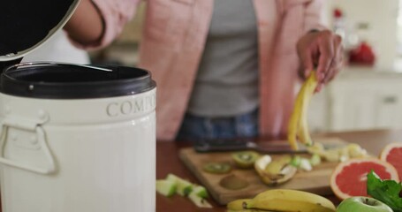 Hands of biracial woman composting vegetable waste in kitchen