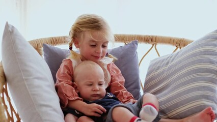 Three years old girl and six months holding on knees her little baby boy, playing.Funny children relationships. Taking care of younger brother, humor concept.
