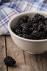 Blackberries in ceramic bowl on rustic wooden background. Selective focus. Shallow depth of field.