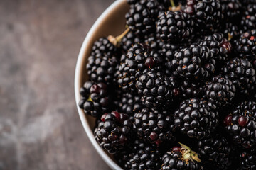 Blackberries in ceramic bowl on rustic wooden background. Selective focus. Shallow depth of field.