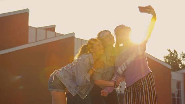 Tilt up of three teenage girls riding on rollerblades taking selfie together with smartphone outside at daytime