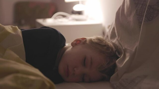 Small boy sleep on bed in room with night light