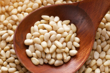 Cleaned pine nuts. Pine nut kernels lie in wooden spoon. Top view of nuts close-up. Advertising photography for marketplaces or online stores.