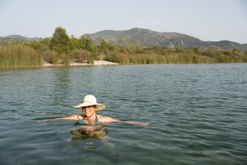 portrait of woman bathing with bikini, chubby white-skinned person in her forties with straw hat with wide eave, natural landscape
