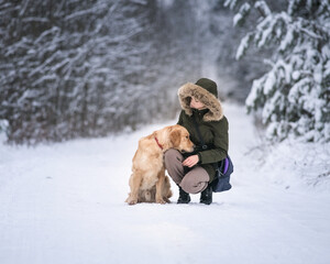 A young beautiful girl playing with a retriever in the winter forest.