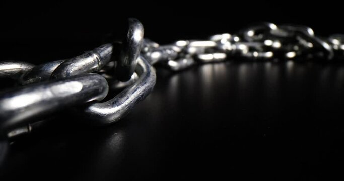 Massive silver chain links made of steel lies on black surface leaving bright reflection. Galvanized massive hard chains for different purposes put in dark studio