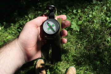 a man holding a compass against the background of green grass got lost in the forest and is looking for a way out