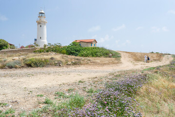 Fototapeta na wymiar Beautiful landscape with white Paphos Lighthouse, blue sky and green grass, white clouds