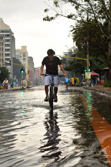 Indigenous Young Man Cycling Through Flooded Bogotá City Streets on Rainy Day