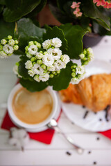 A Perfect Morning Delight: Kalanchoe Flowers, a Cup of Coffee, and a Fresh French Croissant on a Light Table. Breakfast