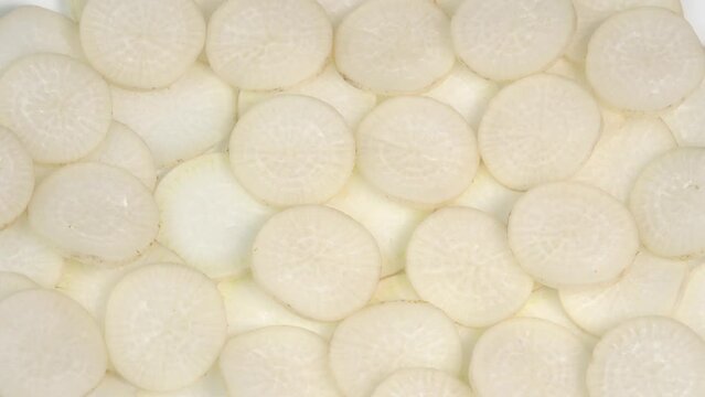 Sliced daikon radish rotates on a plate as a background. Mooli or Daikon, Raphanus sativus, displayed on a market stall, traditional japanese dish