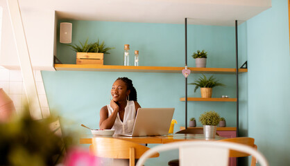 Young black woman drinking coffee  while working on laptop in the cafe