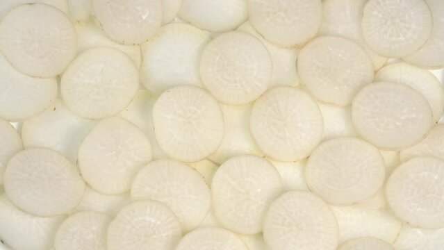 Sliced daikon radish rotates on a plate as a background. Mooli or Daikon, Raphanus sativus, displayed on a market stall, traditional japanese dish