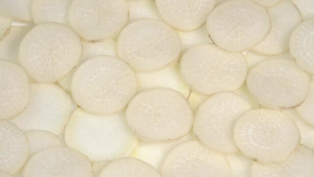 Sliced daikon radish rotates on a plate as a background. Mooli or Daikon, Raphanus sativus, displayed on a market stall, traditional japanese dish