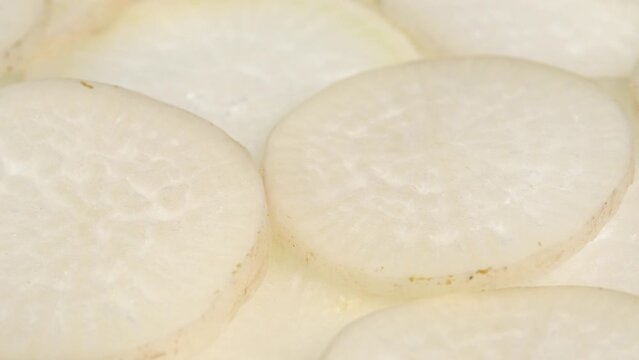 Sliced daikon radish rotates on a plate as a background. Mooli or Daikon, Raphanus sativus, displayed on a market stall, traditional japanese dish