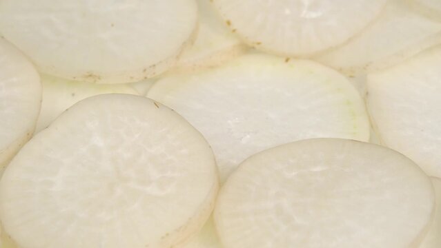 Sliced daikon radish rotates on a plate as a background. Mooli or Daikon, Raphanus sativus, displayed on a market stall, traditional japanese dish