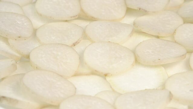 Sliced daikon radish rotates on a plate as a background. Mooli or Daikon, Raphanus sativus, displayed on a market stall, traditional japanese dish