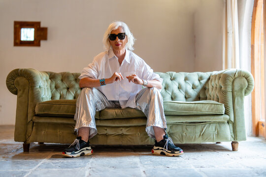 Happy senior woman in sunglasses sitting on sofa and resting in living room
