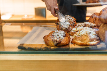 At a bustling bakery, an anonymous worker meticulously restocks a tray of assorted pastries,...