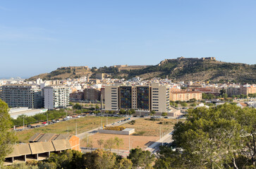 Fototapeta na wymiar Buildings and houses in city, aerial view. Sagunto Castle on mountain. Ruins walls of Fortress Castle at town of Sagunto. Fortress Castillo in Mountains hills. Houses roofs in town at mountains.