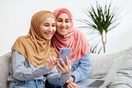 Two Muslim woman wear hijab taking video calling with smartphone, Ramadan celebration concept. Girls waving their hands at the screen smile and are happy to see their family. Vertical image