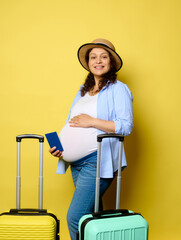 Happy pregnant woman stroking belly, traveling abroad during pregnancy, smiling at camera, isolated yellow background