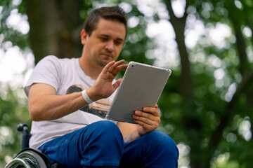 Inclusiveness A man with disabilities in a wheelchair stares intently at the tablet he is holding...
