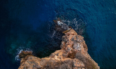 Aerial view of cliffs by the sea. Wave breaking against the rocks. Blue sea with different shades...