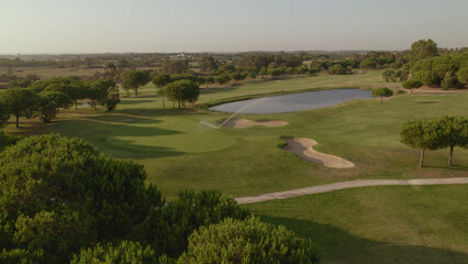 Fototapeta na wymiar Fairway, lake, greens and sand bunker on golf course at sunset. Spain. Aerial view.