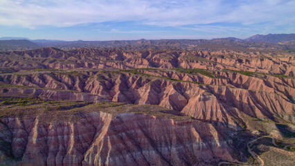 Panoramic aerial view of rocky desert at sunset. Reddish canyons and ravines in arid terrain....
