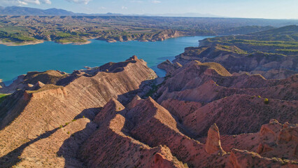 Aerial view over reddish badlands and reservoir at sunset. Panoramic view of ravines and colorful...