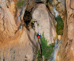 Climbers rappelling down a waterfall. Canyoning descent of the waterfall with climbing equipment. Zenith aerial view. Granada. Andalusia. Spain.