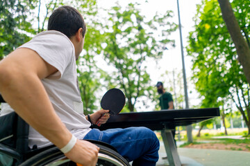 Inclusiveness A disabled man in a wheelchair plays ping pong against an old man with a gray beard...