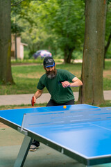 Inclusiveness An elderly focused man with long hair and a gray beard plays ping pong in a city park 